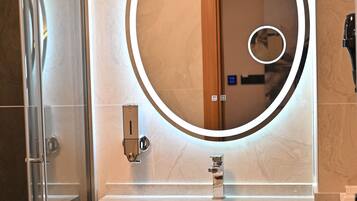 Un baño con tocador moderno, un espejo redondo con iluminación perimetral y cabina de ducha de vidrio.