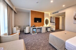 Une chambre d’hôtel comprenant un lit, un bureau avec un miroir, une télévision et un coin salon avec des fauteuils.