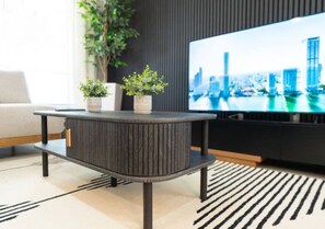 A modern living room with a round, dark-colored coffee table, a flat-screen TV displaying a cityscape, and a striped rug. - Brilliant 3-bedroom house with AC in charming Kissimmee (Kissimmee)