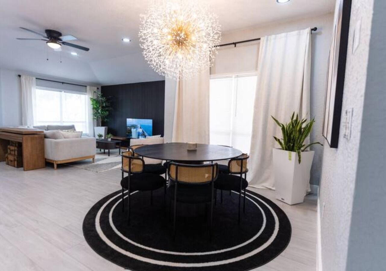 A modern living room with a round dining table, a ceiling fan, and a large window with curtains.