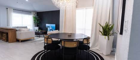 A modern living room with a round dining table, a ceiling fan, and a large window with curtains.