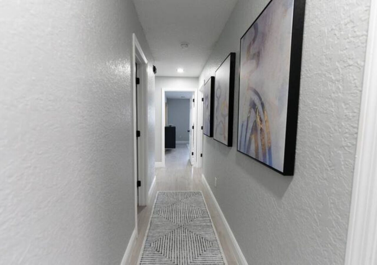 A hallway with a patterned rug, white walls, and framed artwork.