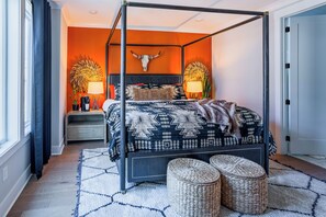 Een hemelbed met een deken met een geometrisch patroon, twee nachtkastjes met lampen, een aan de muur bevestigde decoratie van een stierenhoofd en een geweven vloerkleed.