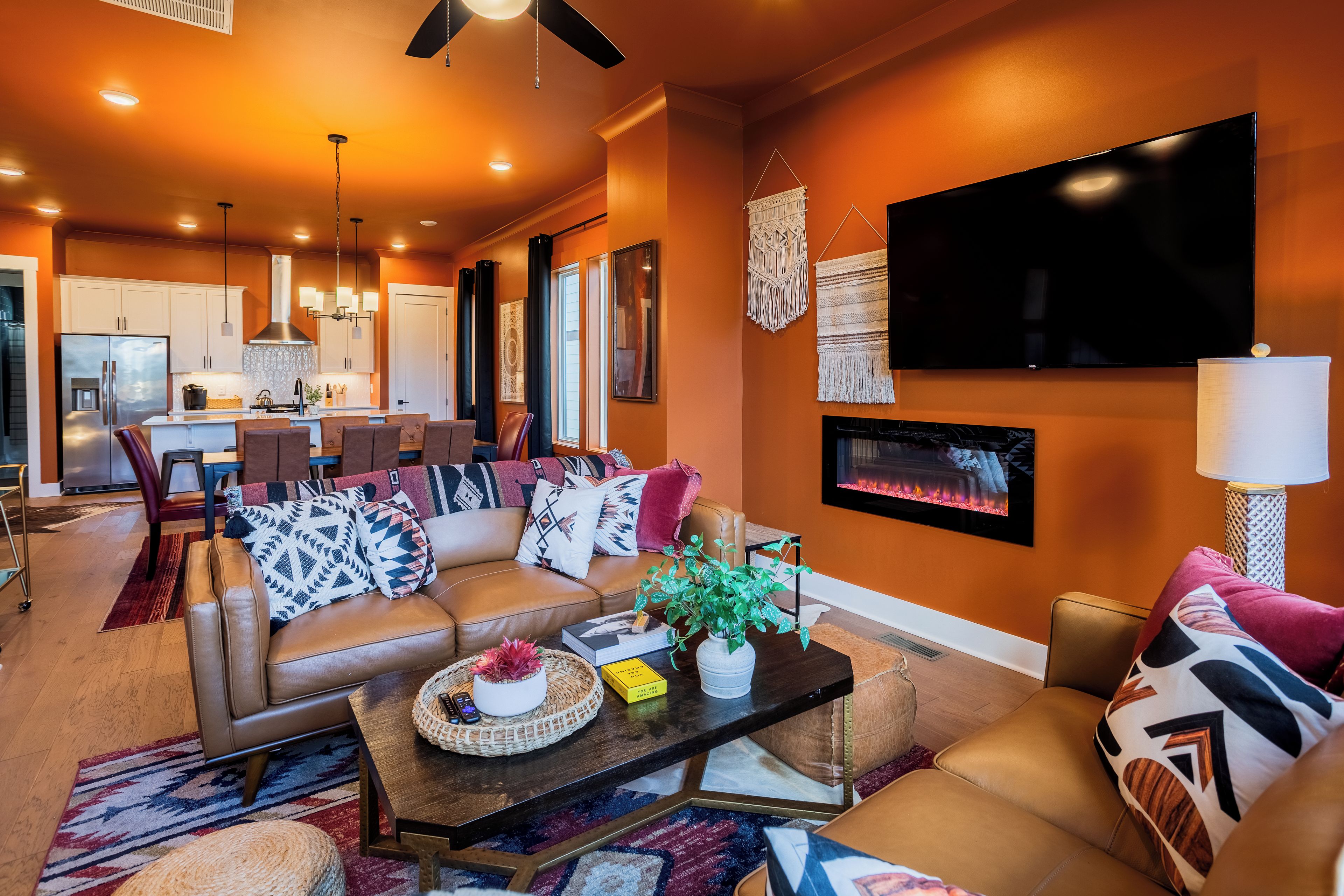 A modern living room with a fireplace, a television, and a dining area with a kitchen in the background.