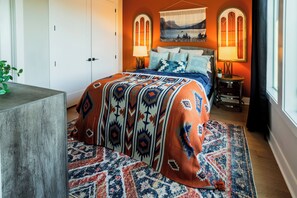 A bedroom with a bed, two bedside lamps, a tapestry, and a window with curtains. - The Wild West - Nashville: Rooftop Deck (Nashville)