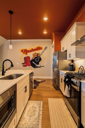 A modern kitchen with white cabinets, a stainless steel refrigerator, and a gas stove. - The Wild West - Nashville: Rooftop Deck (Nashville)