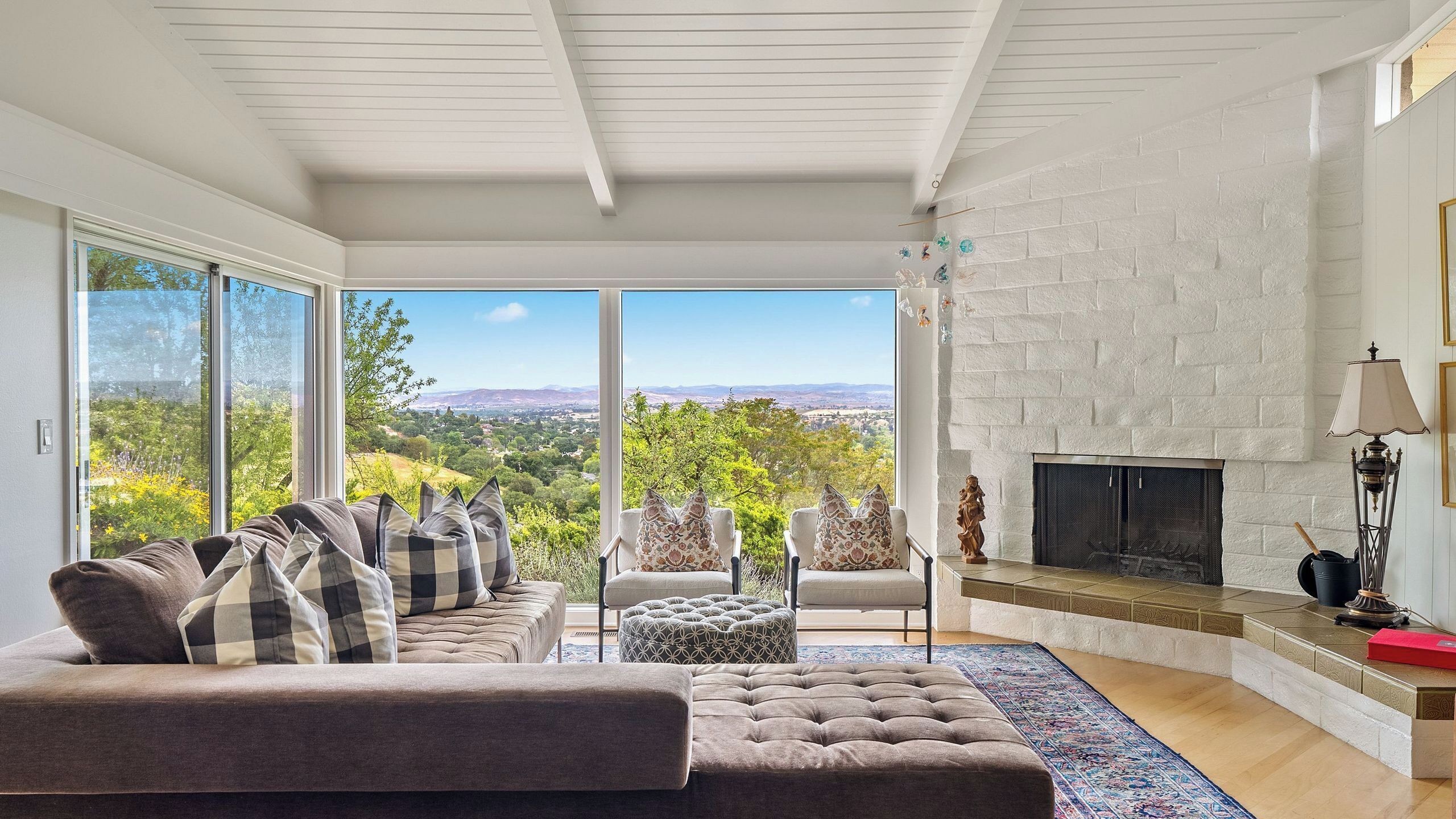 A modern living room with a fireplace, a sofa set, and a view of a green landscape.