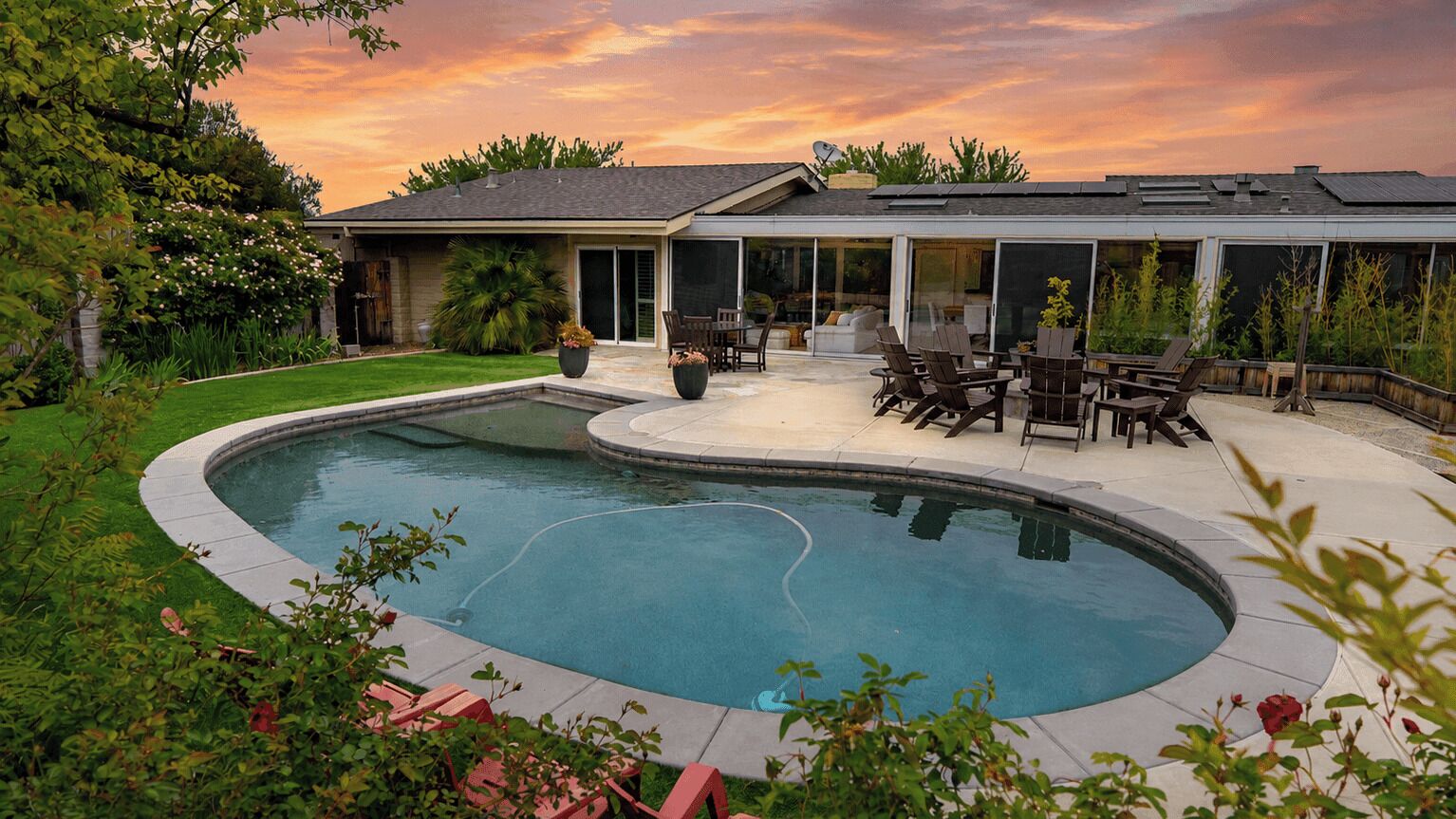 Une maison moderne dotée d’une piscine, de mobilier de jardin et d’un jardin bien entretenu.