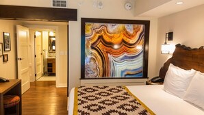 A hotel room with a large abstract painting, a patterned bedspread, and a wooden headboard. - Orlando | Family Lodge Retreat | Pool + Resort | 2BR (Lake Buena Vista)