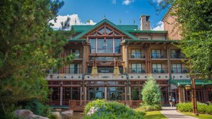 A multi-story lodge with a prominent entrance, large windows, and a well-maintained garden with a small stream. - Orlando | Family Lodge Retreat | Pool + Resort | 2BR (Lake Buena Vista)