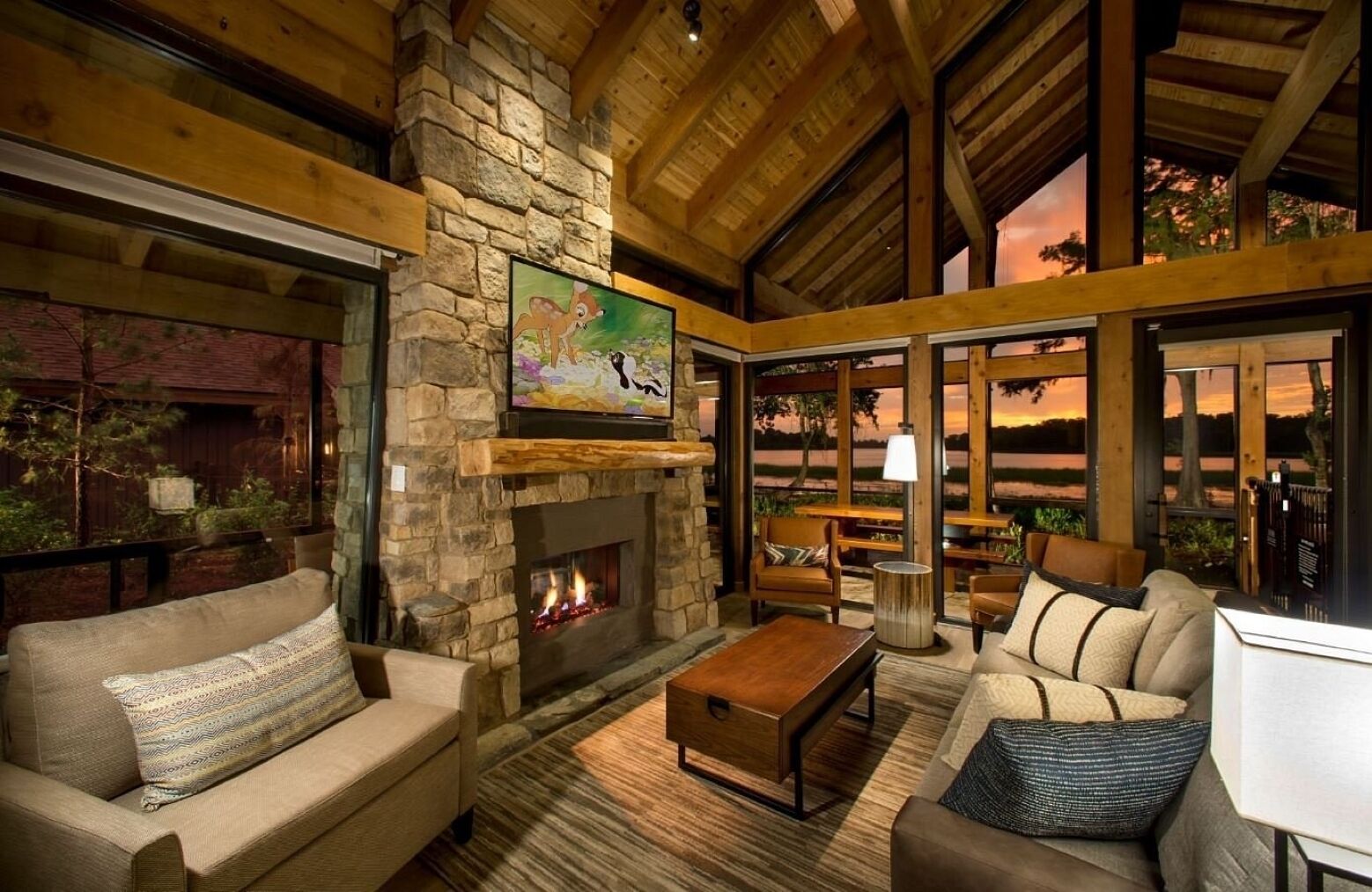 A cozy interior with a stone fireplace, comfortable seating, and large windows offering a view of the outdoors.