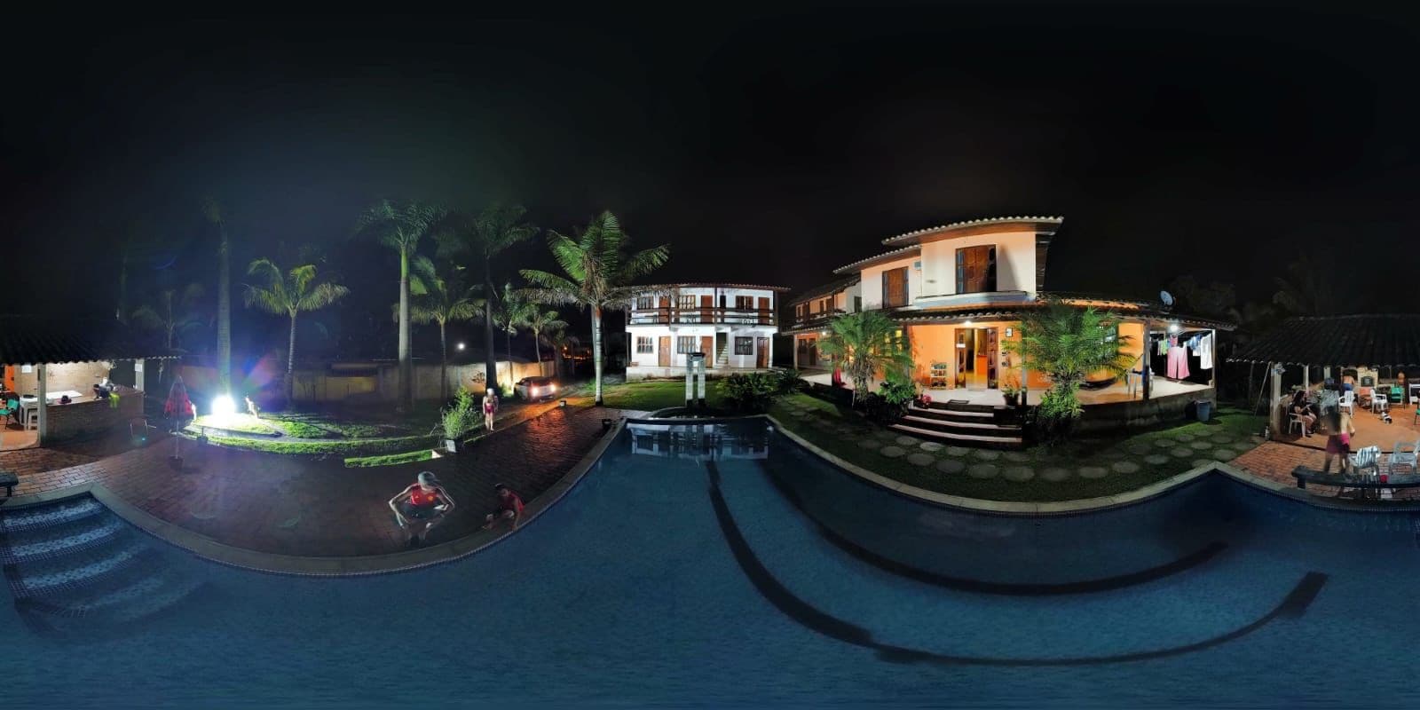 A nighttime view of a resort with a swimming pool, palm trees, and a well-lit building.