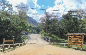 A dirt road leading to a camping area with a wooden bridge and signs indicating amenities like a restaurant and WiFi.