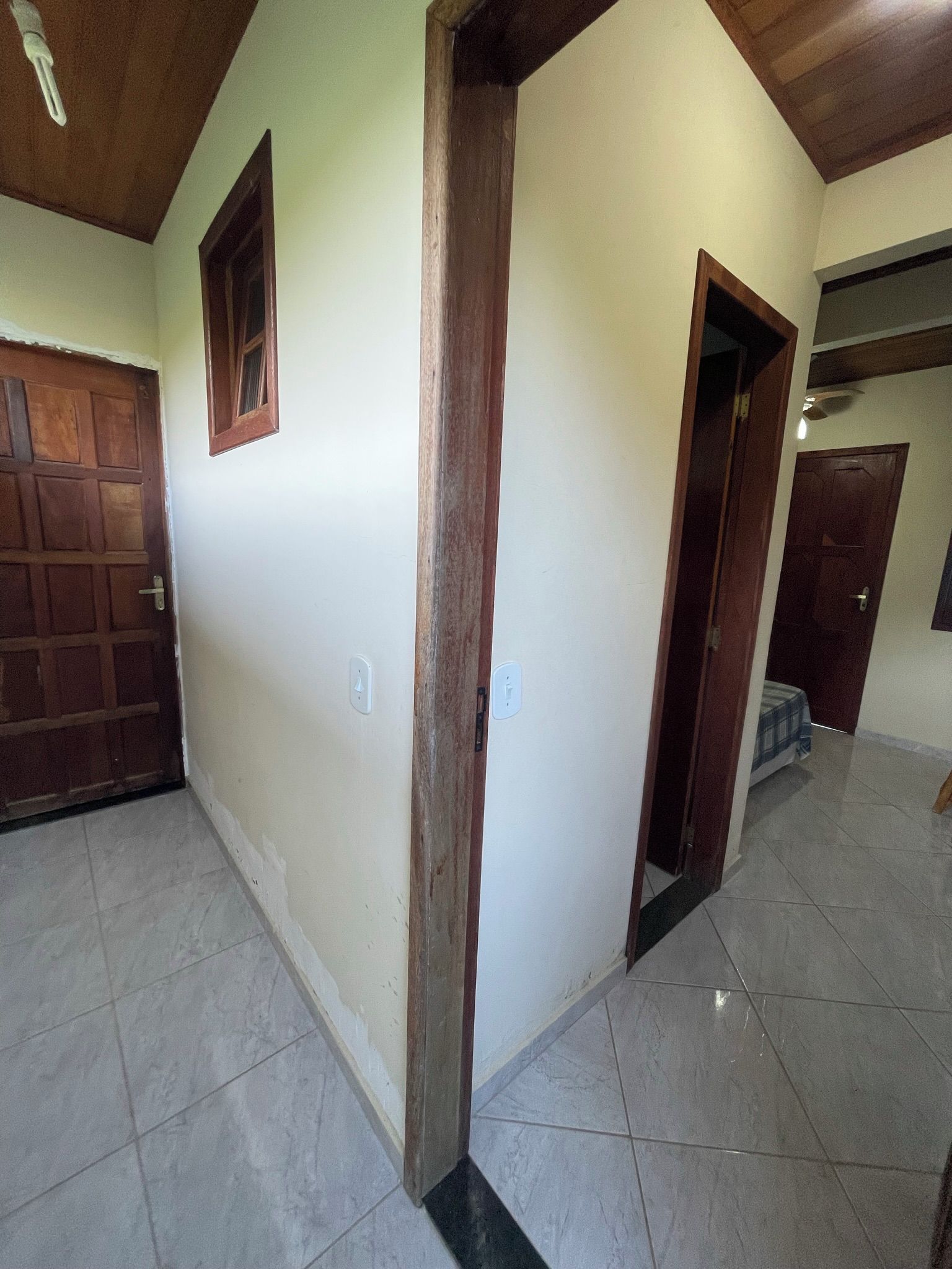 Un pasillo con suelo de baldosas, una puerta de madera y un ventanal pequeño.