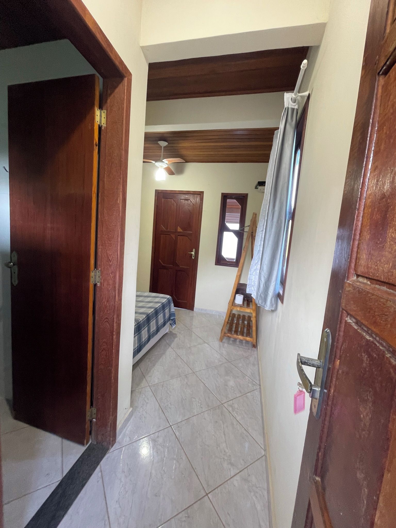 Un pasillo con una cama, una puerta de madera, un ventilador de techo y una ventana.