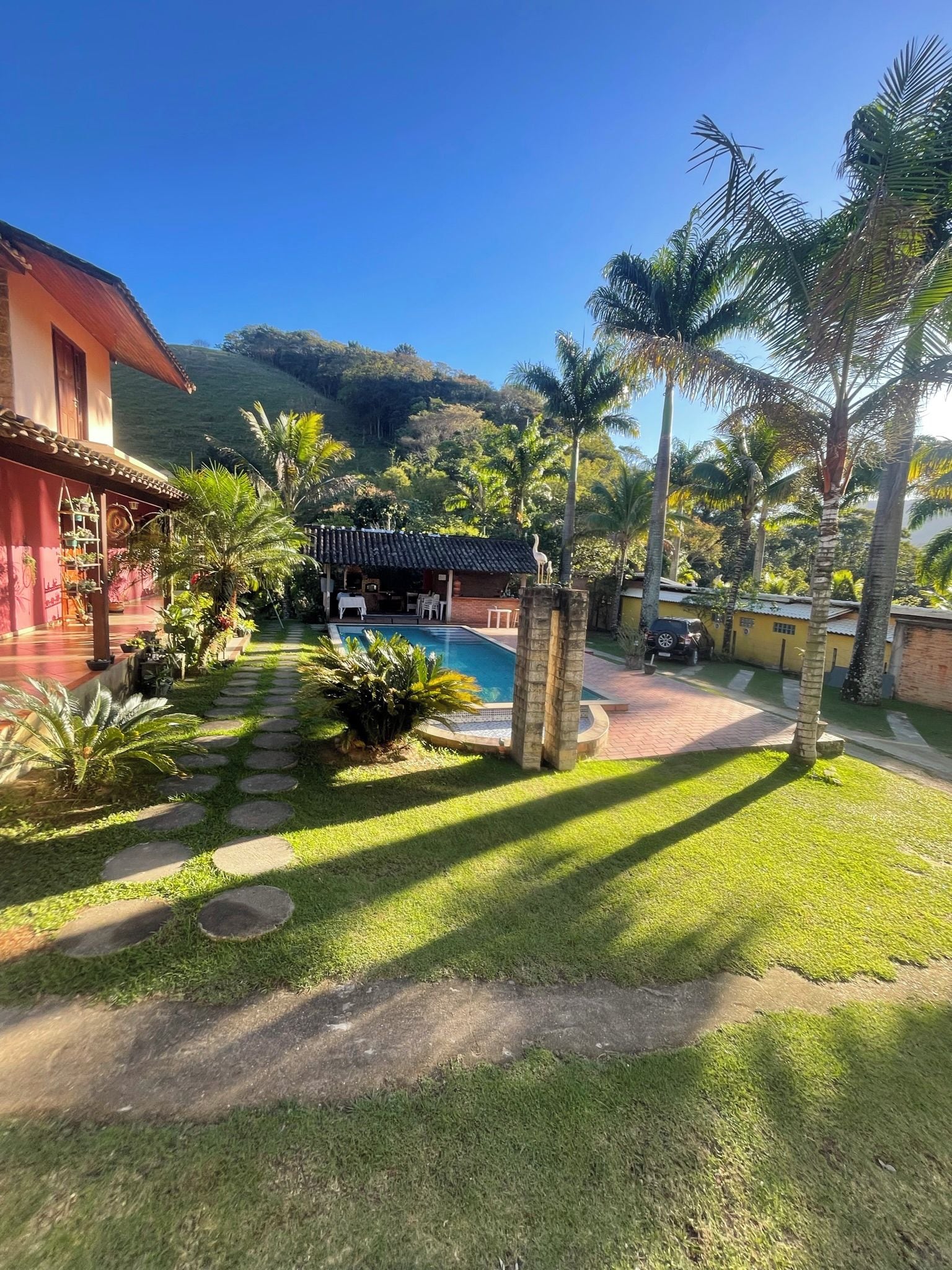 Área residencial com piscina, palmeiras e uma casa de fachada vermelha.