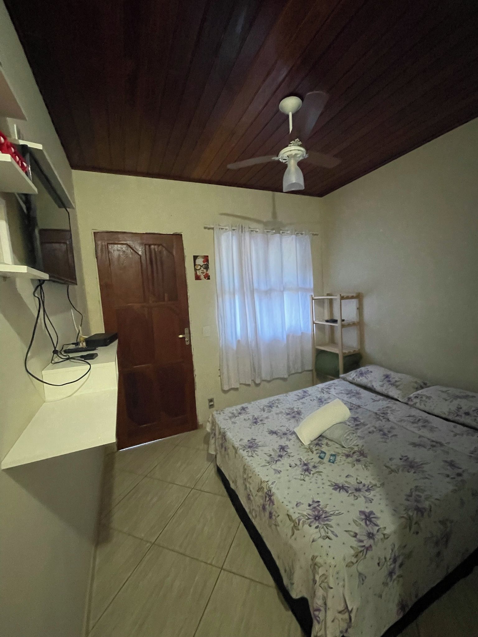 A bedroom with a bed, a ceiling fan, a door, and a window with curtains.