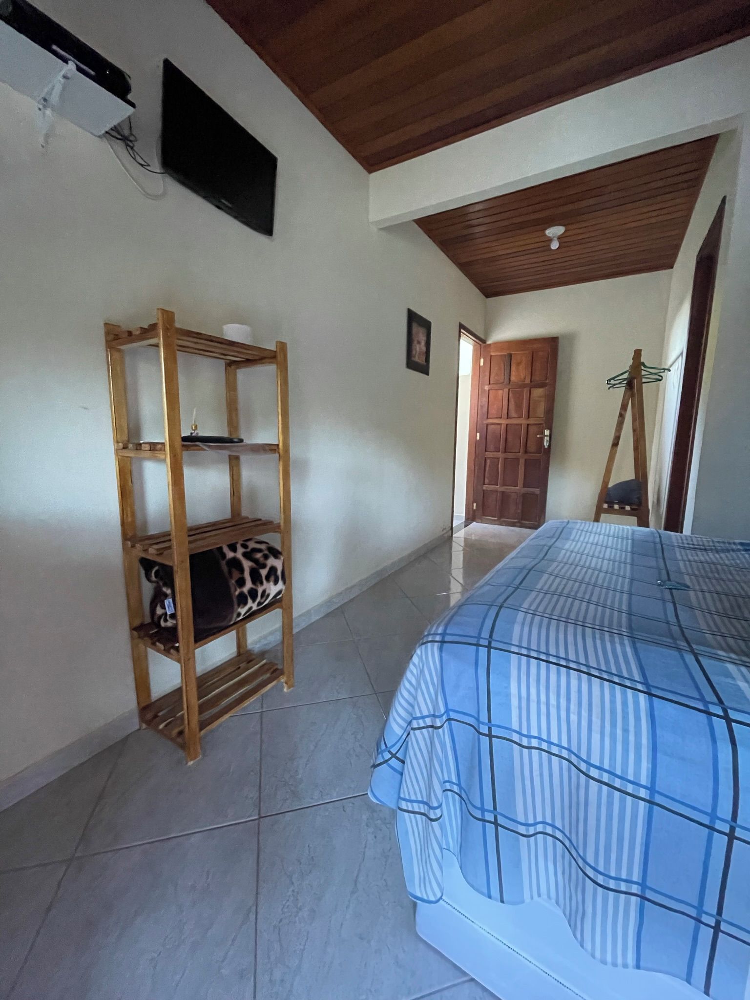 Un dormitorio con una cama, un estante de madera con un cojín estampado de leopardo, una puerta de madera y una escalera apoyada en la pared.