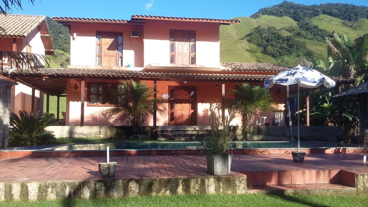 Edificio de dos plantas con techo de tejas, piscina y jardín con plantas en macetas.