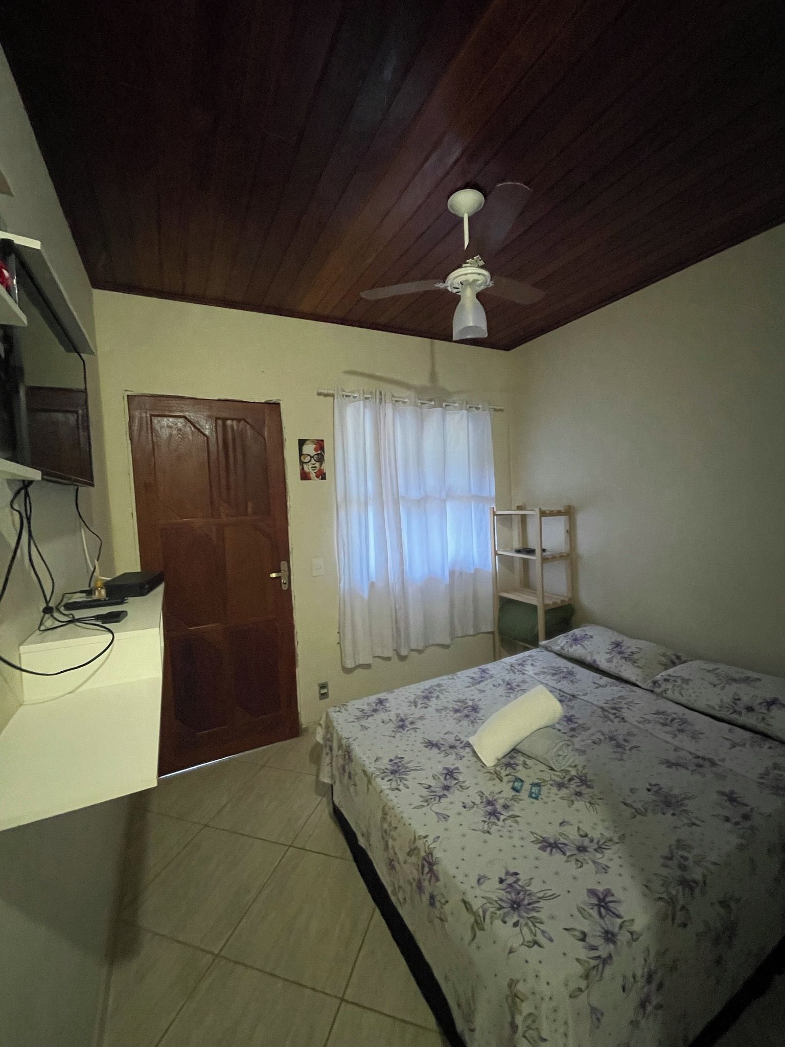 A bedroom with a bed, a ceiling fan, a door, and a small shelf.