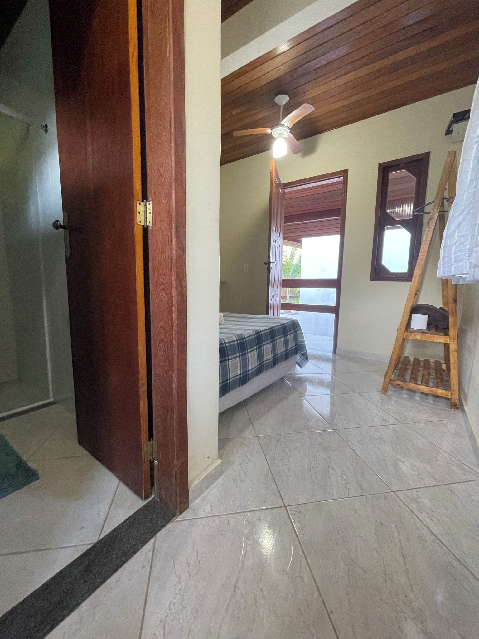 Une pièce avec un lit, une échelle en bois, un ventilateur de plafond et une porte.