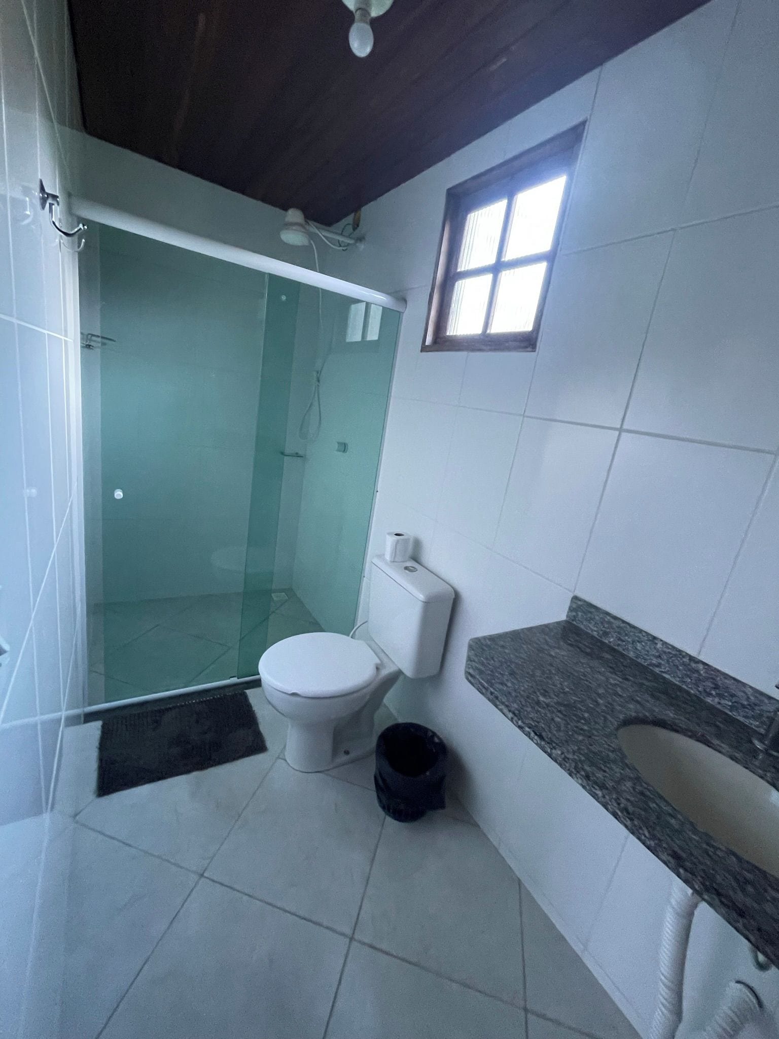 A bathroom with a glass-enclosed shower, a toilet, a sink with a granite countertop, and a window.
