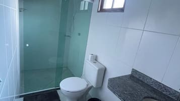 A bathroom with a glass-enclosed shower, a toilet, a sink with a granite countertop, and a window.