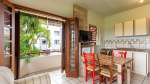 A compact kitchen with a dining area, a television, and a view of a building with balconies. - Apt 270m From the Beach in Floripa-sc Stcy202 (Florianópolis)
