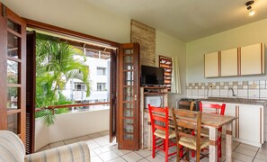 A compact kitchen with a dining area, a television, and a view of a building with balconies. - Apt 270m From the Beach in Floripa-sc Stcy202 (Florianópolis)