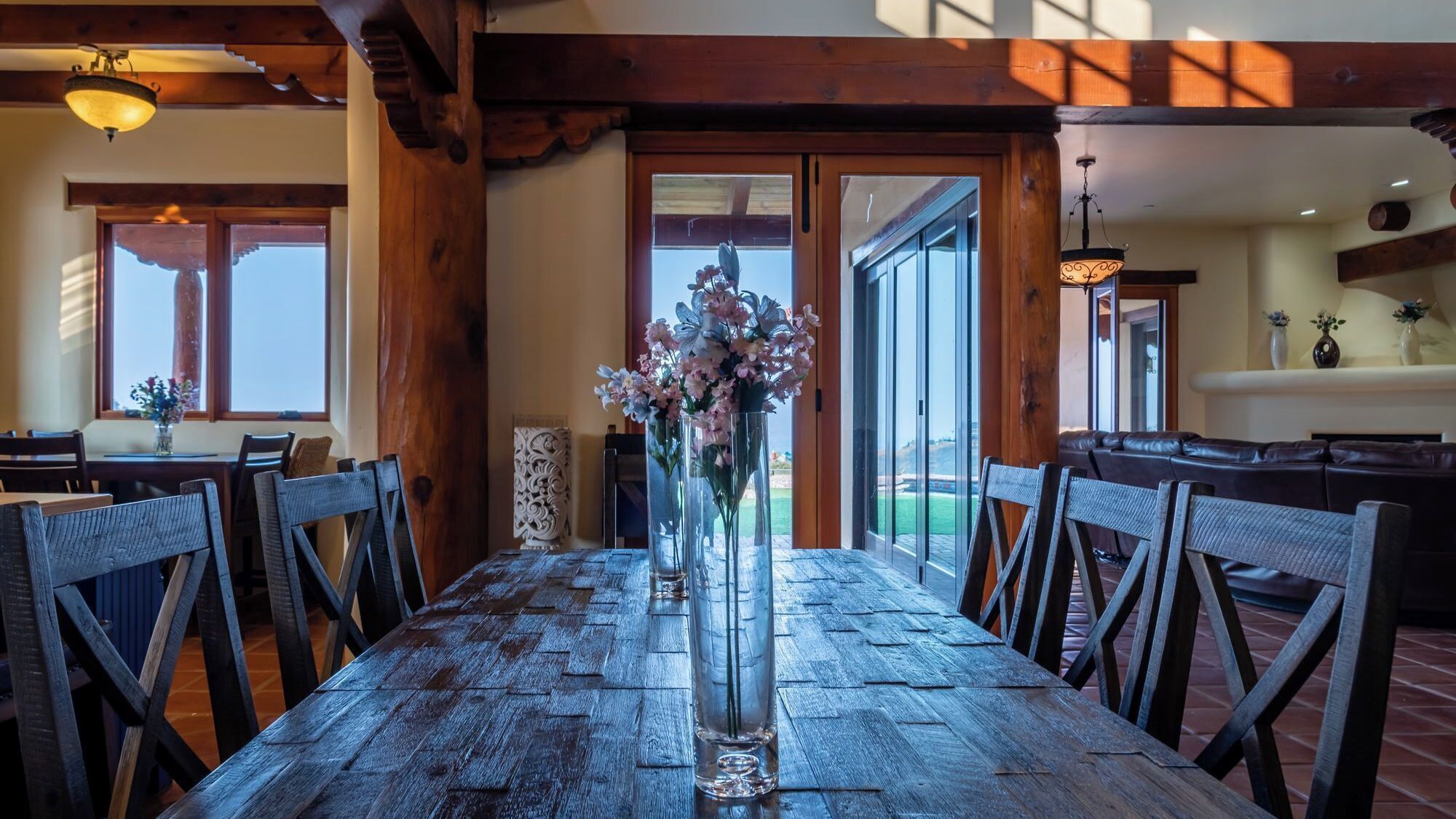 A wooden dining table with chairs, a vase of flowers, and a view through a glass door to an outdoor area.