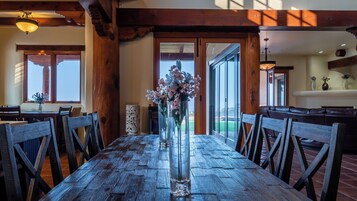 Una mesa de comedor de madera con sillas, un jarrón de flores y vistas al exterior a través de un ventanal.