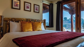 Una cama con cabecera de madera, dos almohadas y una colcha roja. Encima de la cama, hay tres cuadros enmarcados en la pared.