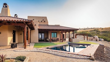 Una casa moderna con piscina, mobiliario exterior y vistas a las colinas.