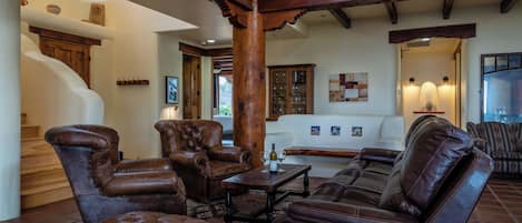 Amplia sala de estar con muebles de cuero, una escalera y vistas al exterior.