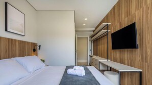 A modern hotel room with a bed, bedside table, a flat-screen TV, and a wooden panel wall. - Apartment With Barbecue in Condo With Pool Tso0403 (Balneário Camboriú)