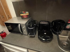 Eine Küchenarbeitsplatte mit einer Mikrowelle, einer Kaffeemaschine und einer Schachtel Jacobs Espresso-Kapseln.