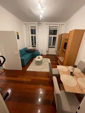 Ein gemütlicher Wohnraum mit einer Couch, einem Esstisch mit Platzsets, einem kleinen Teppich und einer Deckenleuchte.