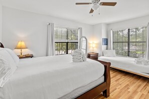 Ein Hotelzimmer mit einem großen Bett, einem kleineren Bett, einem Deckenventilator und zwei Fenster mit Jalousien.
