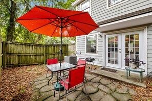 Eine Terrasse mit Tisch und Stühlen, einem roten Sonnenschirm und einem Grill.