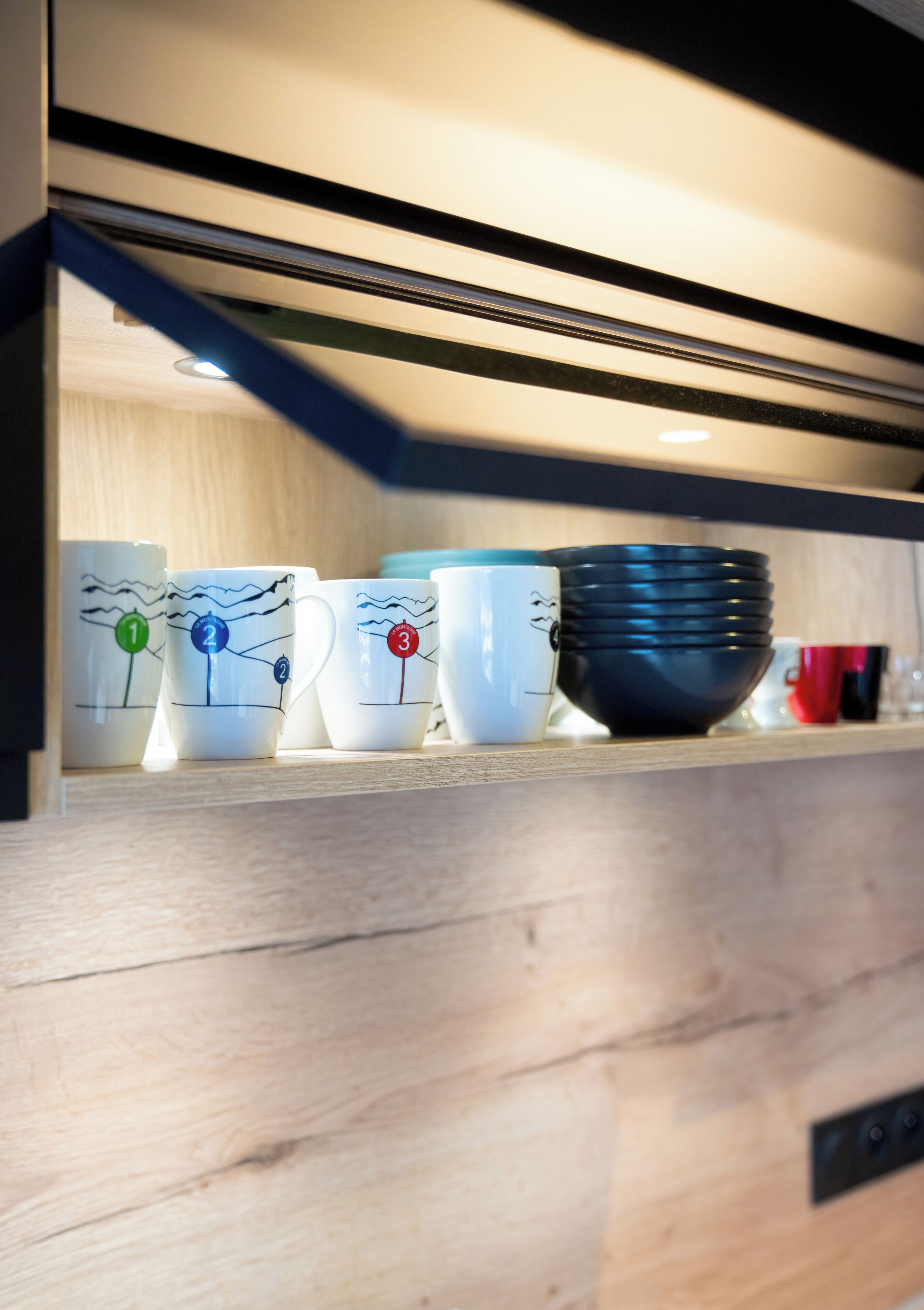 A kitchen counter with a stack of white mugs, each marked with a number, and a black bowl.