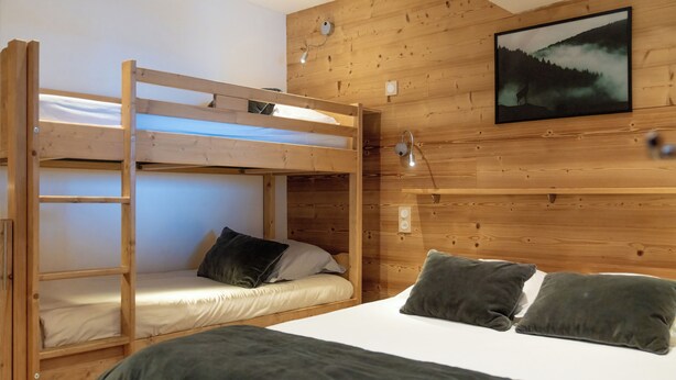 A bunk bed room with a wooden headboard, a bedside table, and a wall-mounted lamp.