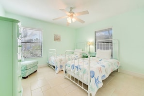 A room with two beds, a ceiling fan, a bedside table with a lamp, and a window with blinds. - Captiva Beach Home w/ Gulf Views & Resort Access (Captiva)