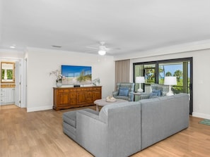 A modern living room with a grey sectional sofa, a wooden cabinet, a television, and a view of the outdoors through a sliding glass door. - Dune-Side Home w/ Loft & Dual Sound Views (Captiva)