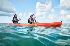 Dos personas remando en kayak en un mar tranquilo con cielo despejado.