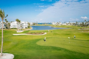 A golf course with a water hazard, palm trees, and buildings in the background. - Elegant Gulf-View Home | Resort Access Included (Captiva)