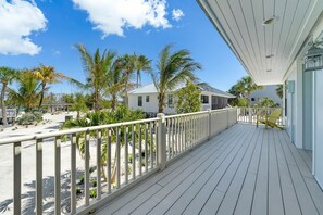 A wooden deck with a railing, palm trees, and a clear sky. - Beachfront Home w/ Screened Lanai & Pool Access (Captiva)