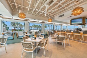 A spacious indoor dining area with high ceilings, large windows, and a bar area.