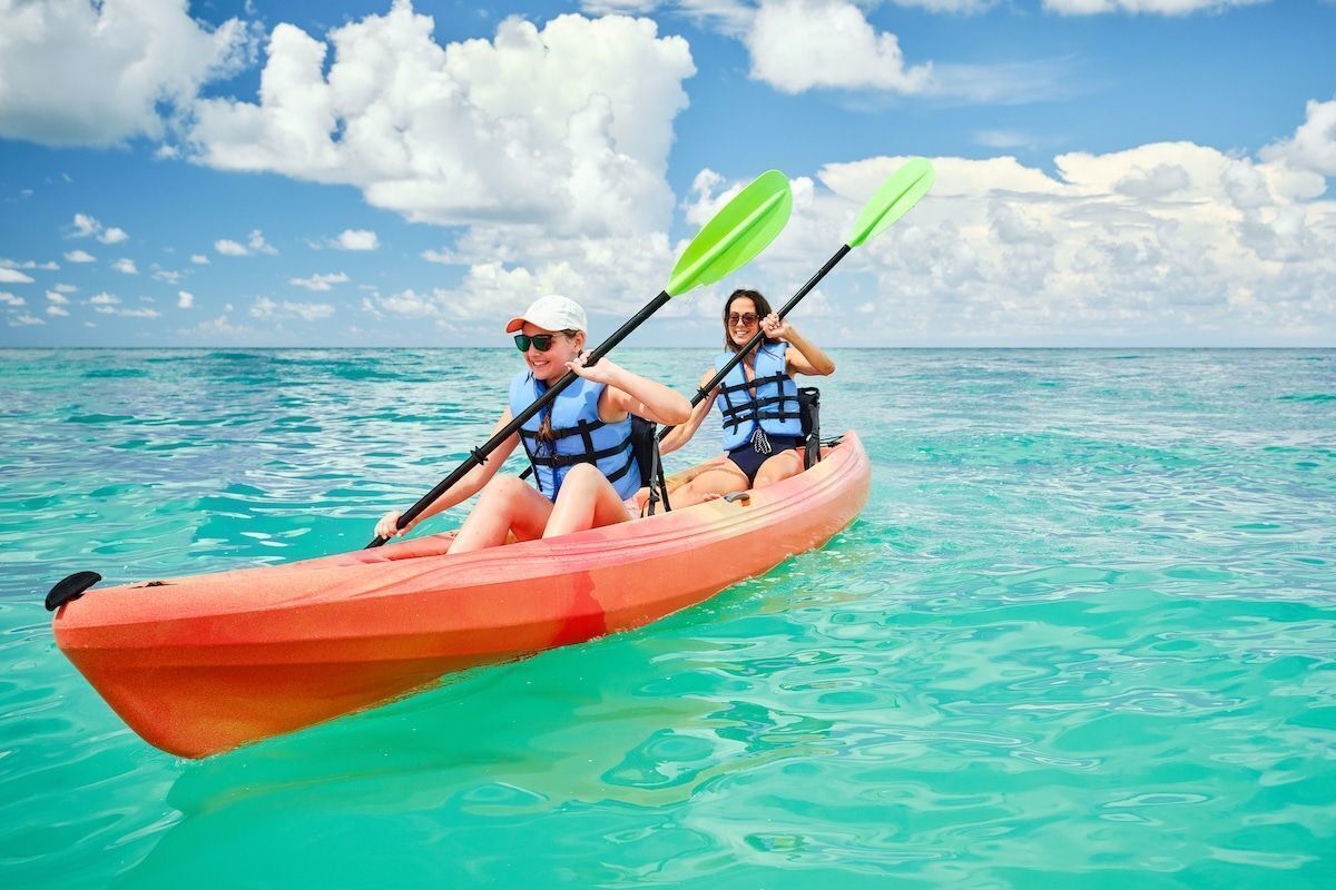 Zwei Personen in einem kleinen, orangefarbenen Kajak auf klarem, türkisblauem Wasser.