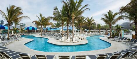 A pool area with multiple lounge chairs and umbrellas, surrounded by palm trees.