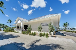 Ein modernes Strandhaus mit einer überdachten Terrasse, Palmen und blauem Himmel.